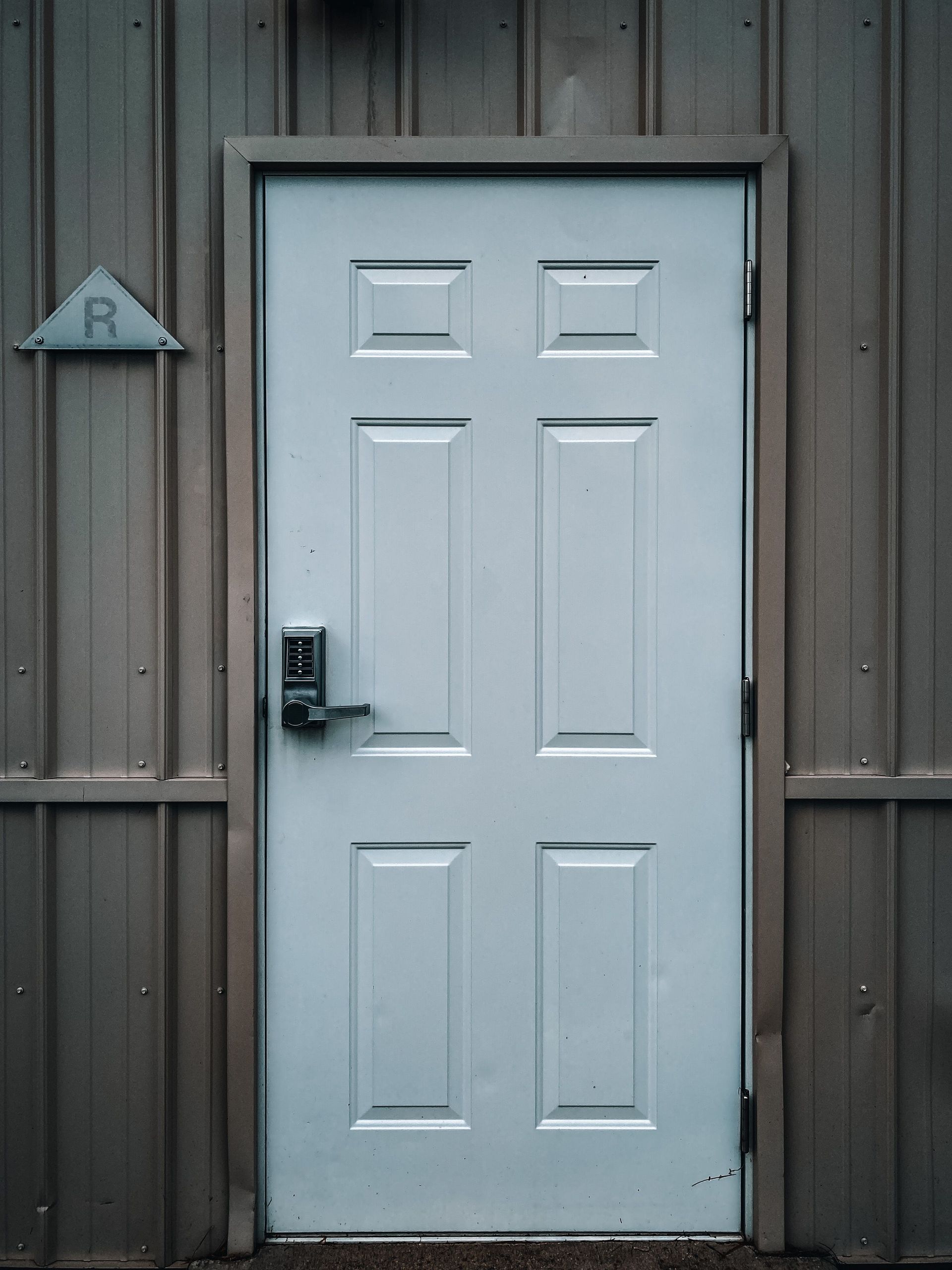 Closed white door with modern electronic lock placed in building with grey walls in daytime